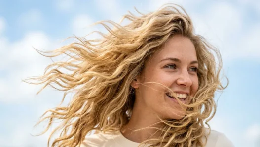 Woman with blonde wavy hair caught in natural wind movement showing individual strand texture and golden highlights