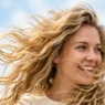 Woman with blonde wavy hair caught in natural wind movement showing individual strand texture and golden highlights