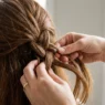 Close-up of feminine hands braiding hair strands together with bright lighting showing technique