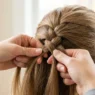 Close-up of feminine hands creating a three-strand braid in textured hair with bright lighting