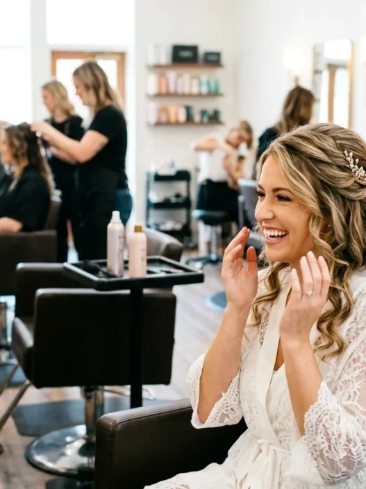 Woman admiring her finished bridal half up half down hairstyle with stylist standing behind her