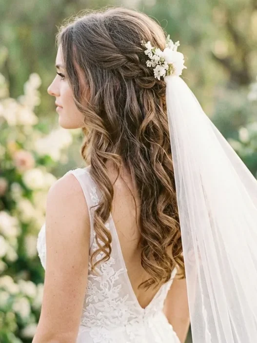 Bride with romantic half up half down hairstyle and flowing veil in outdoor setting