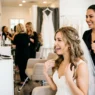 Bride admiring her finished romantic wedding hair down style with hair stylist standing behind her in bright salon
