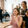 Bridesmaid seeing her new haircut for first time in salon mirror with stylist behind her
