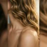 Collarbone length hair with golden waves cascading over bare shoulder showing natural movement and dimension