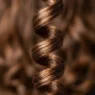 Close-up macro view of a single defined spiral curl showing hair cuticle reflection and texture