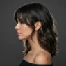 Woman with textured shoulder-length hair showing curtain bangs and face-framing layers in profile view