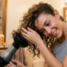 Woman using diffuser attachment on blow dryer to style thin curly hair with lifting motion