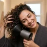 Woman using diffuser attachment on blow dryer to style thin curly hair with head tilted sideways