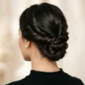 Elegant low chignon updo from behind showing twisted hair sections at the nape with pearl earrings visible