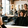 Woman with fresh French bob cut admiring her reflection in salon mirror with stylist behind her