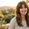 Woman showing contrast between face-framing layers and curtain bangs in golden natural lighting