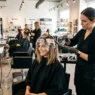Professional stylist applying balayage color to woman's lob-length hair with foil placement in bright salon