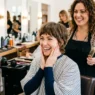 Woman with delighted expression admiring her fresh Wendy cut in salon mirror with stylist standing behind her