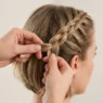 Feminine hands braiding short bob hair with three strands being interwoven in bright natural lighting
