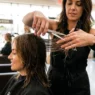 Professional hair stylist cutting layered shag hairstyle on female client in bright salon setting