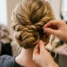 Stylist's hands threading bobby pin into twisted curly updo section at nape of neck