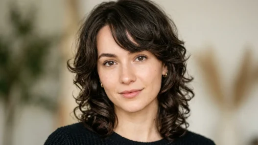 Woman with prominent forehead showing textured side-swept bangs and face-framing layers in soft beauty lighting