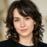 Woman with prominent forehead showing textured side-swept bangs and face-framing layers in soft beauty lighting