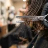 Extreme close-up of thinning shears cutting through layered hair with fragments falling and gloved hand visible
