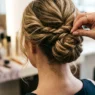 Stylist's fingers threading bobby pin into twisted hair section during updo creation process