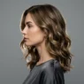 Woman with wavy lob hairstyle shown in elegant side profile against neutral studio background