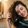 Woman using diffuser attachment on blow dryer to scrunch curly hair with head tilted sideways