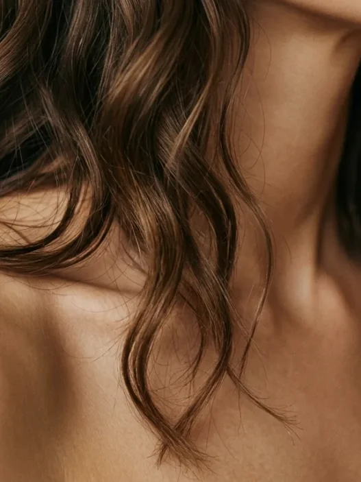 Woman with collarbone length wavy hair cascading over bare shoulder showing natural movement