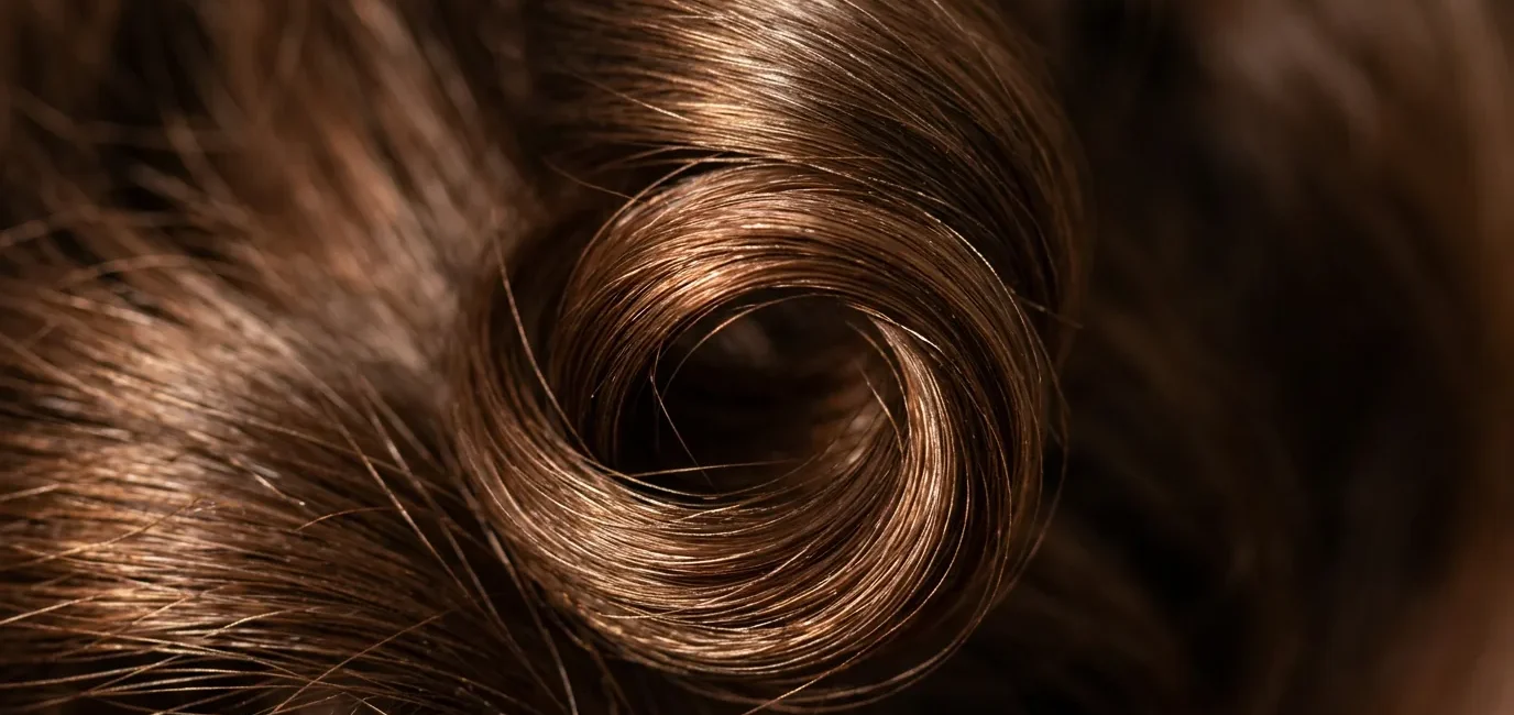 Extreme close-up of single spiral curl showing light reflecting off hair cuticle with shallow depth of field