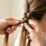 Close-up of feminine hands weaving three hair strands in braiding motion with detailed finger positioning