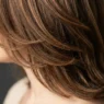 Woman with perfectly layered shoulder-length hair showing subtle highlights from jawline to crown