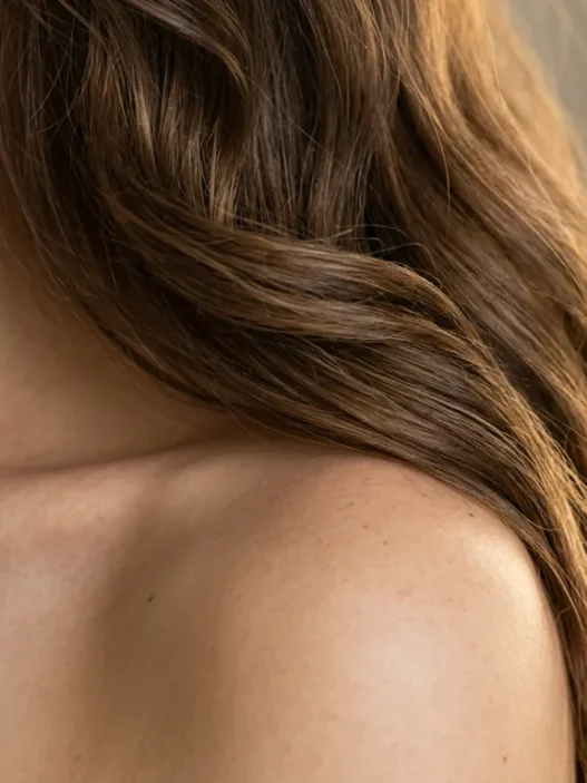 Long wavy hair cascading over bare shoulder showing natural movement and golden highlights