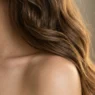 Long wavy hair cascading over bare shoulder showing natural movement and golden highlights