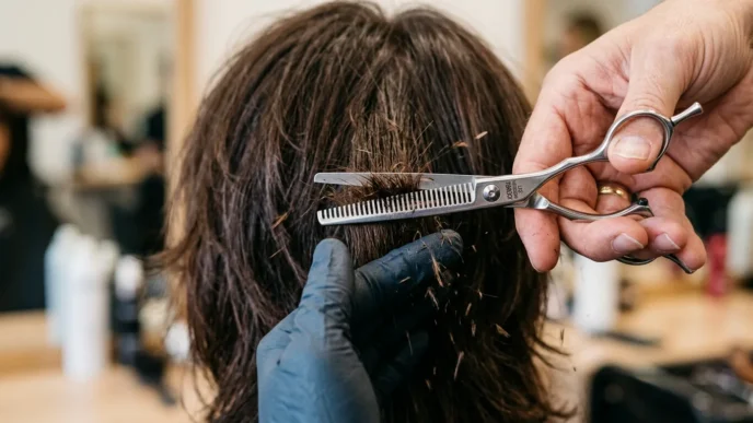 Professional stylist's hands using thinning shears on layered hair with fragments falling during precise cutting technique