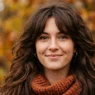 Woman with full 70s shag haircut and curtain fringe in deep brunette against warm autumn bokeh background
