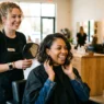 Woman admiring her new shoulder-length lob haircut in salon mirror with stylist standing behind her proudly