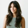 Woman with long dark brown 90s layered blowout and curtain bangs in bright studio light