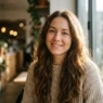 Woman with long chestnut loose waves standing by a bright cafe window with soft side light