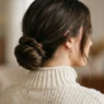 Woman with low twisted bun at nape wearing cream sweater in soft studio light
