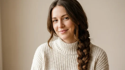 Woman with long brown hair in cozy winter braid smiling softly in neutral studio light