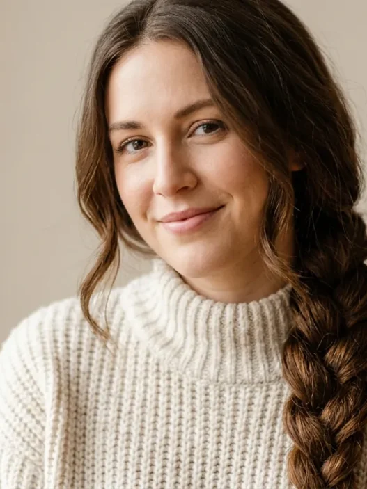 Woman with long brown hair in cozy winter braid smiling softly in neutral studio light