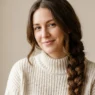 Woman with long brown hair in cozy winter braid smiling softly in neutral studio light