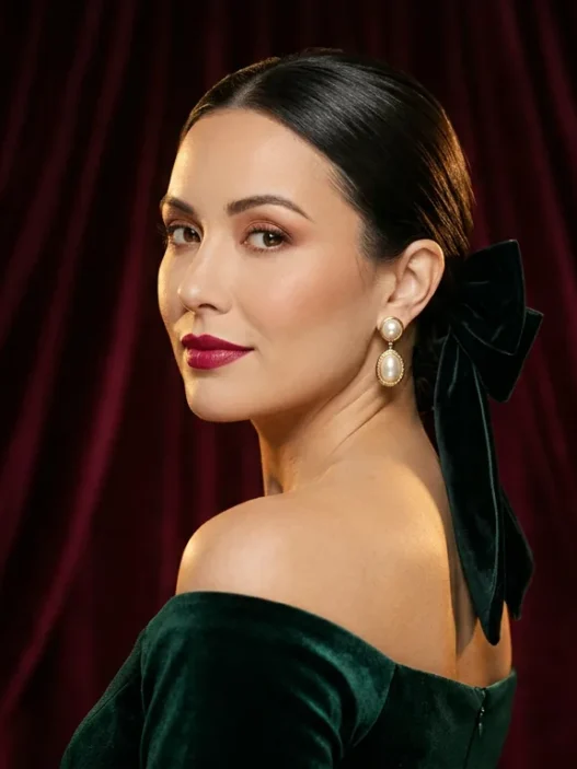 Woman with sleek low chignon and velvet bow in formal portrait against burgundy backdrop