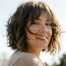 Woman with chin-length shaggy French bob and curtain bangs with hair moving in breeze under bright sky