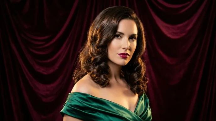 Woman with medium glossy brunette holiday waves posing against burgundy velvet backdrop in studio light