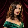 Woman with medium glossy brunette holiday waves posing against burgundy velvet backdrop in studio light