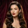 Woman with long glossy holiday waves and side part against burgundy velvet backdrop in studio light