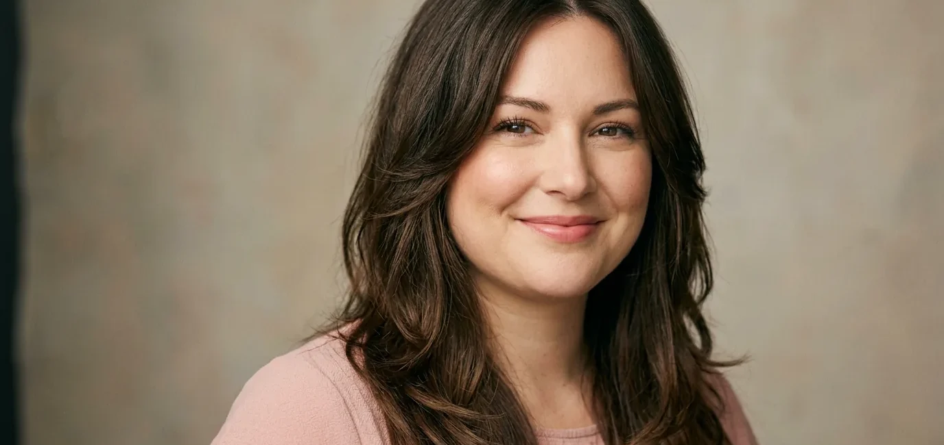 Woman with long layered brown hair parted off-center framing her face in soft studio light