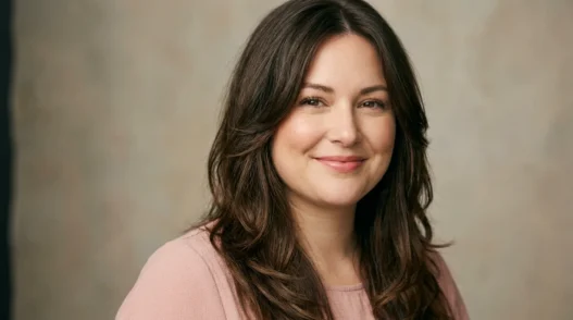 Woman with long layered brown hair parted off-center framing her face in soft studio light