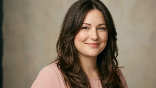 Woman with long layered brown hair parted off-center framing her face in soft studio light